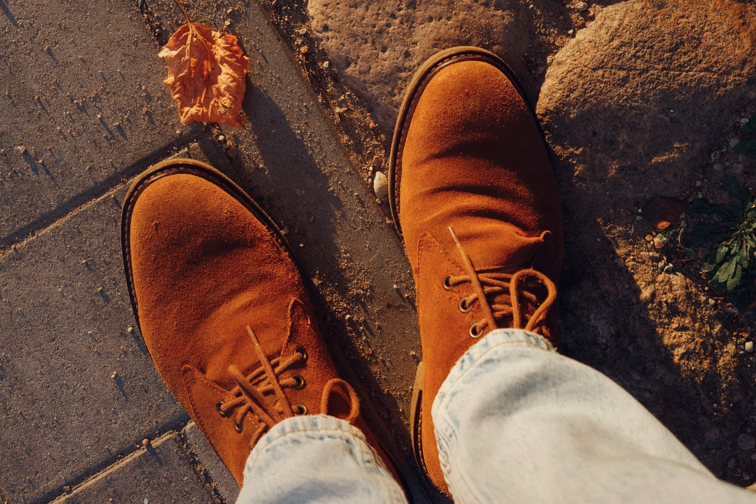 Braune Wildlederstiefel und leichte Jeans auf Kopfsteinpflaster.